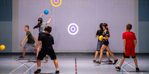 Children playing wall ball using a 3D camera projectors in a gym